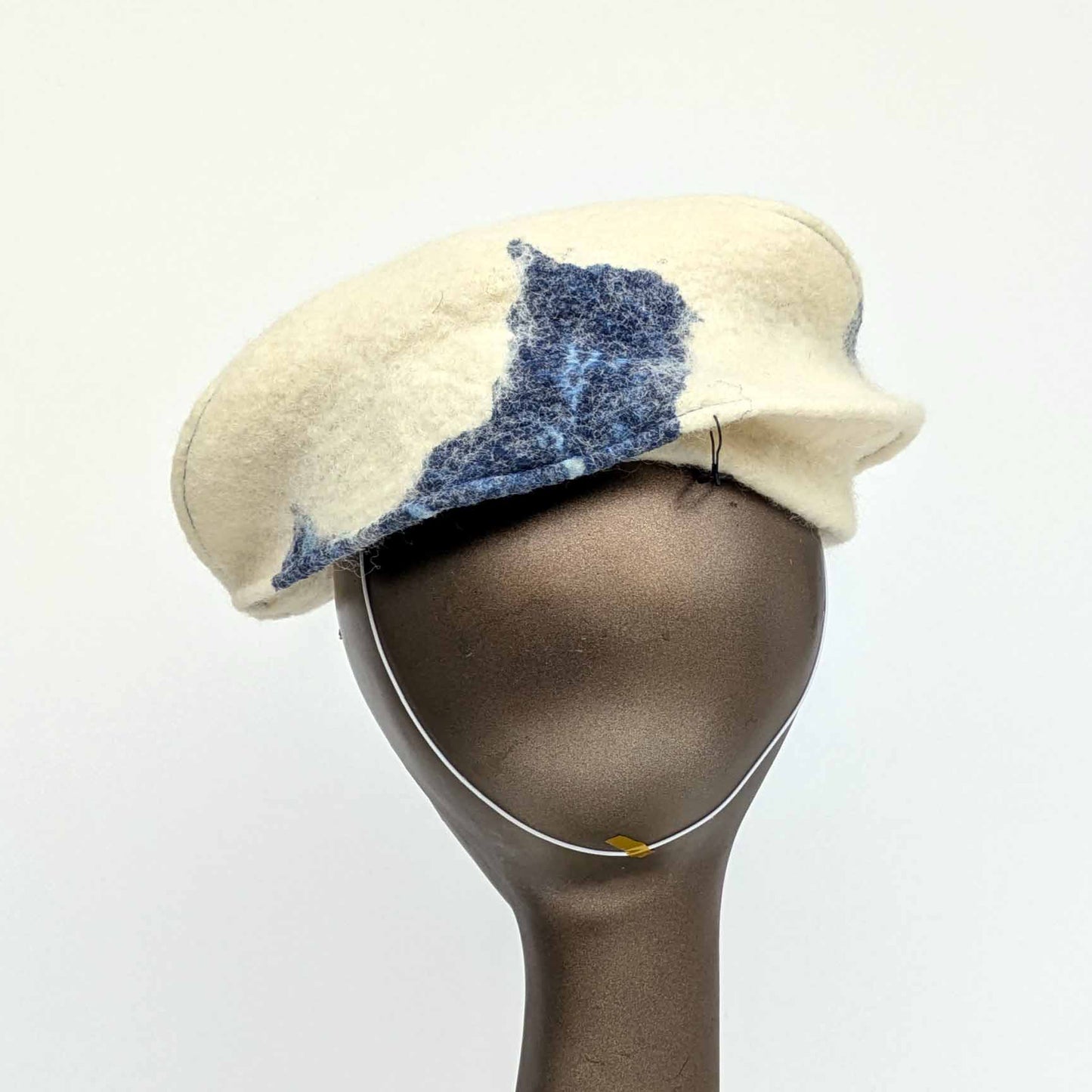 Cream coloured fascinator with blue cyanotype decorative pattern - worn on a mannequin - backview - with millinery elastic worn at nape of neck.