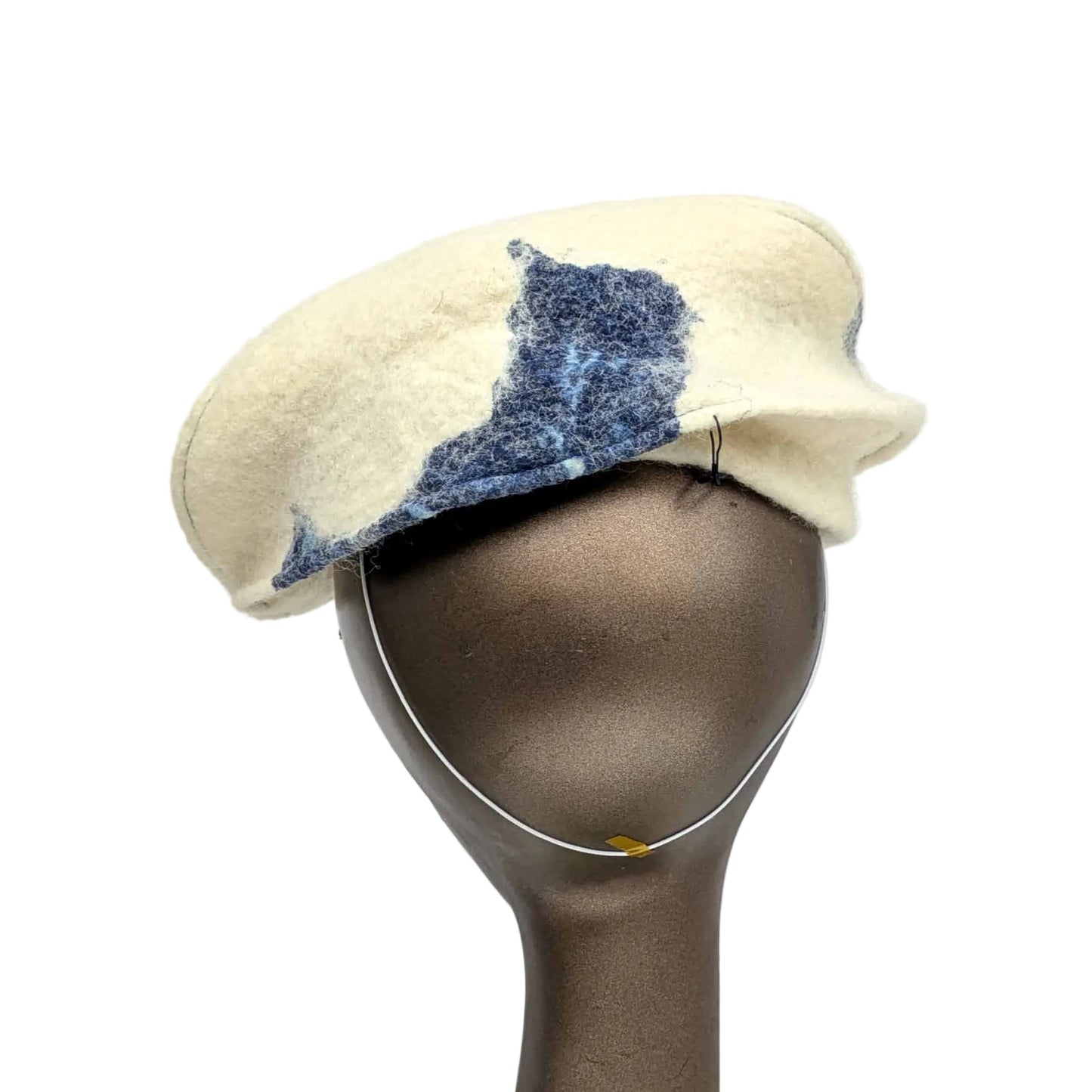 Cream coloured fascinator with blue cyanotype decorative pattern - worn on a mannequin - backview - with millinery elastic worn at nape of neck.