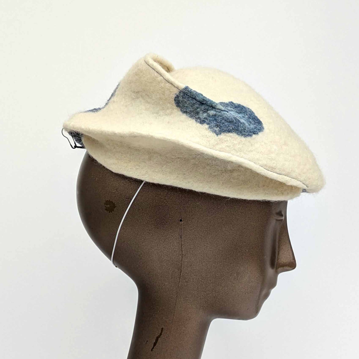 Cream coloured fascinator with blue cyanotype decorative pattern - worn on a mannequin - side view.