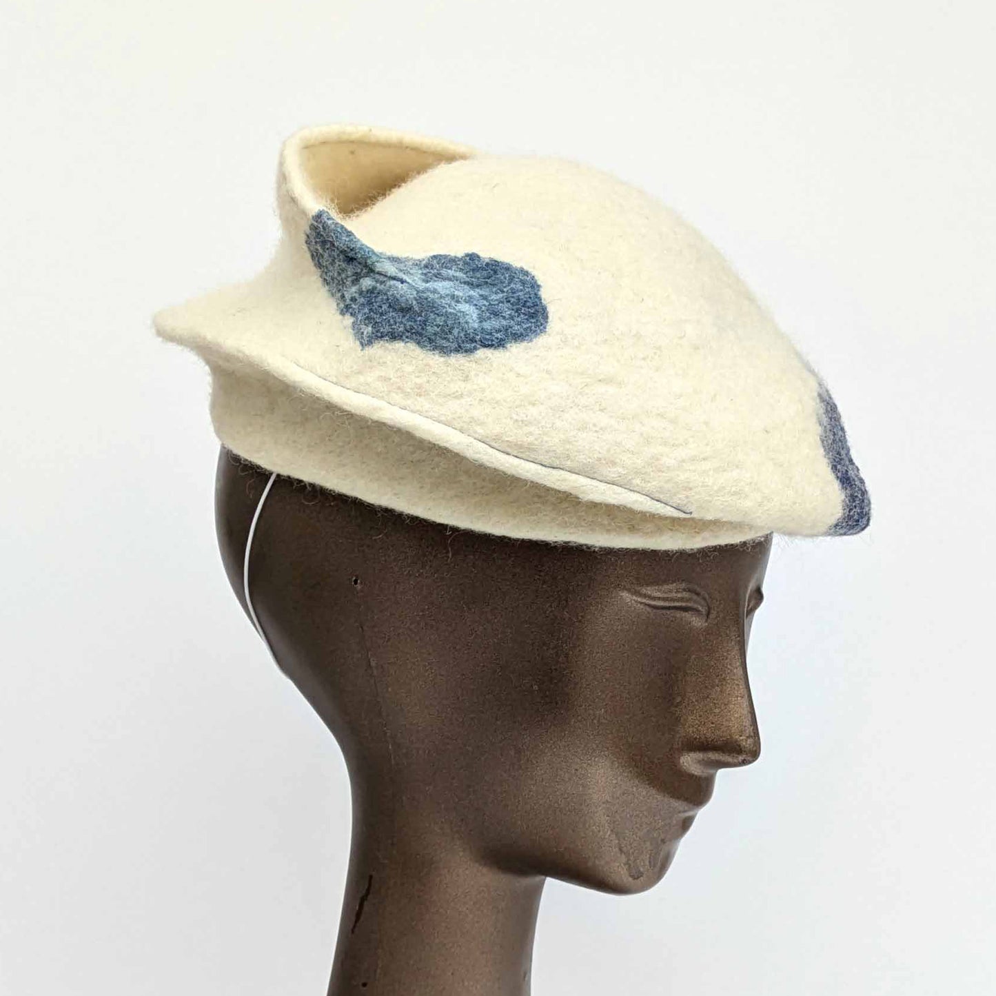 Cream coloured fascinator with blue cyanotype decorative pattern - worn on a mannequin - threequartersview