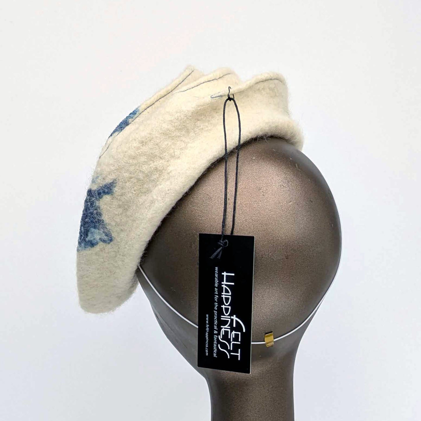 Cream coloured felt fascinator with topstitching and blue seaweed patterning on the top. Back view, with millinery elastic at the nape.