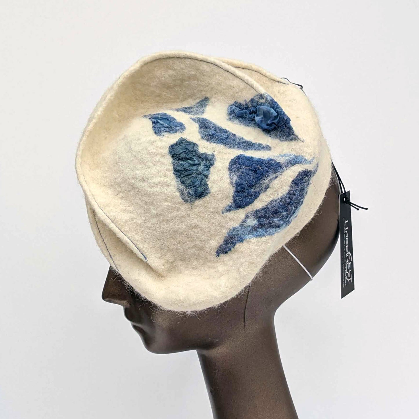 Cream coloured felt fascinator with topstitching and blue seaweed patterning on the top. Side view.