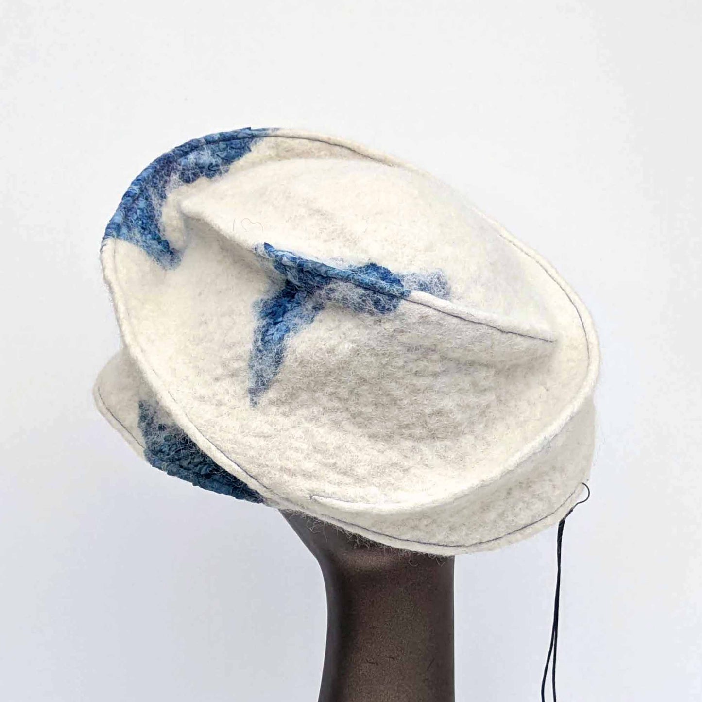 White asymmetrical brimmed cap with seaweed cyanotype printed blue silk decorations. Back view.