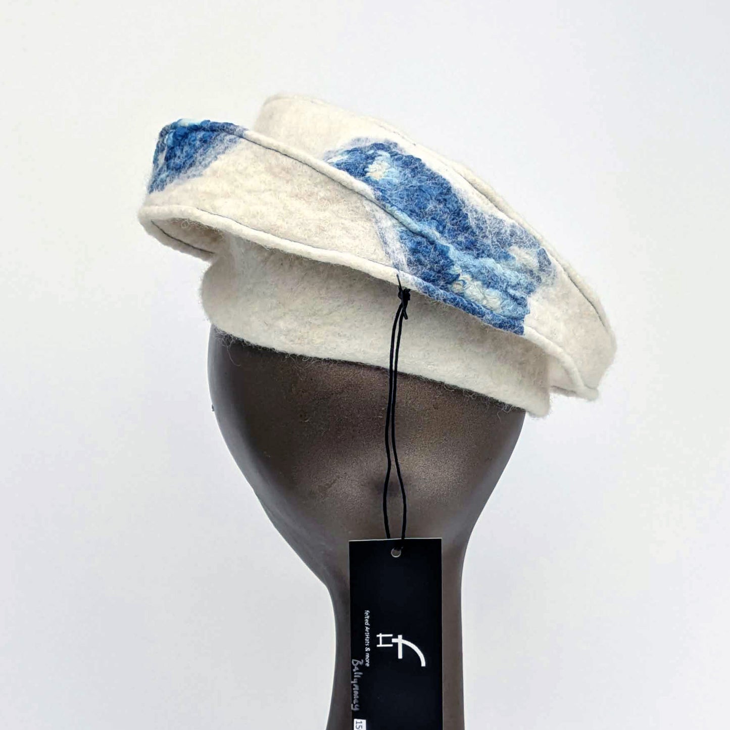 Cream-coloured fascinator hat with blue seaweed cyanotype printed accents on a mannequin head against a white background -backview