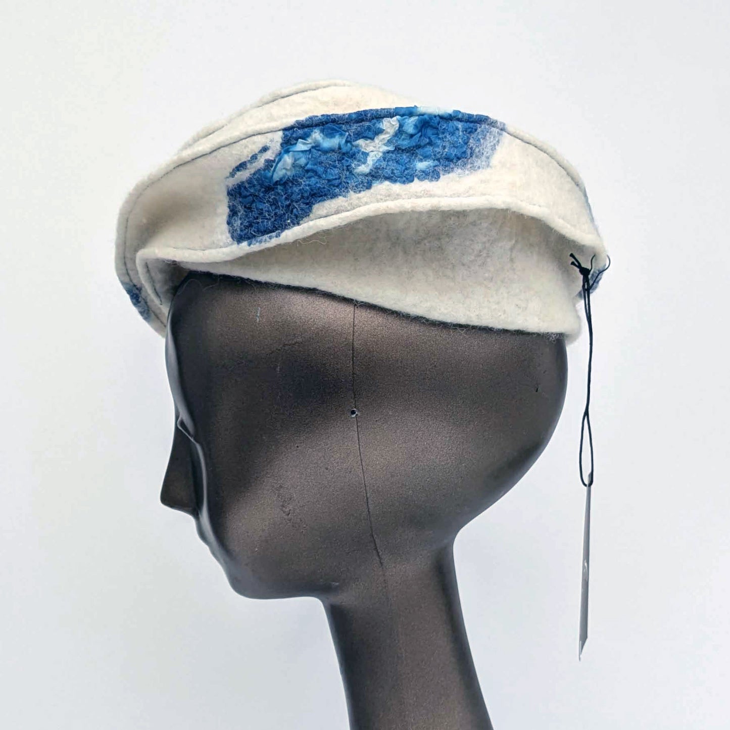 Cream-coloured fascinator hat with blue seaweed cyanotype printed accents on a mannequin head against a white background