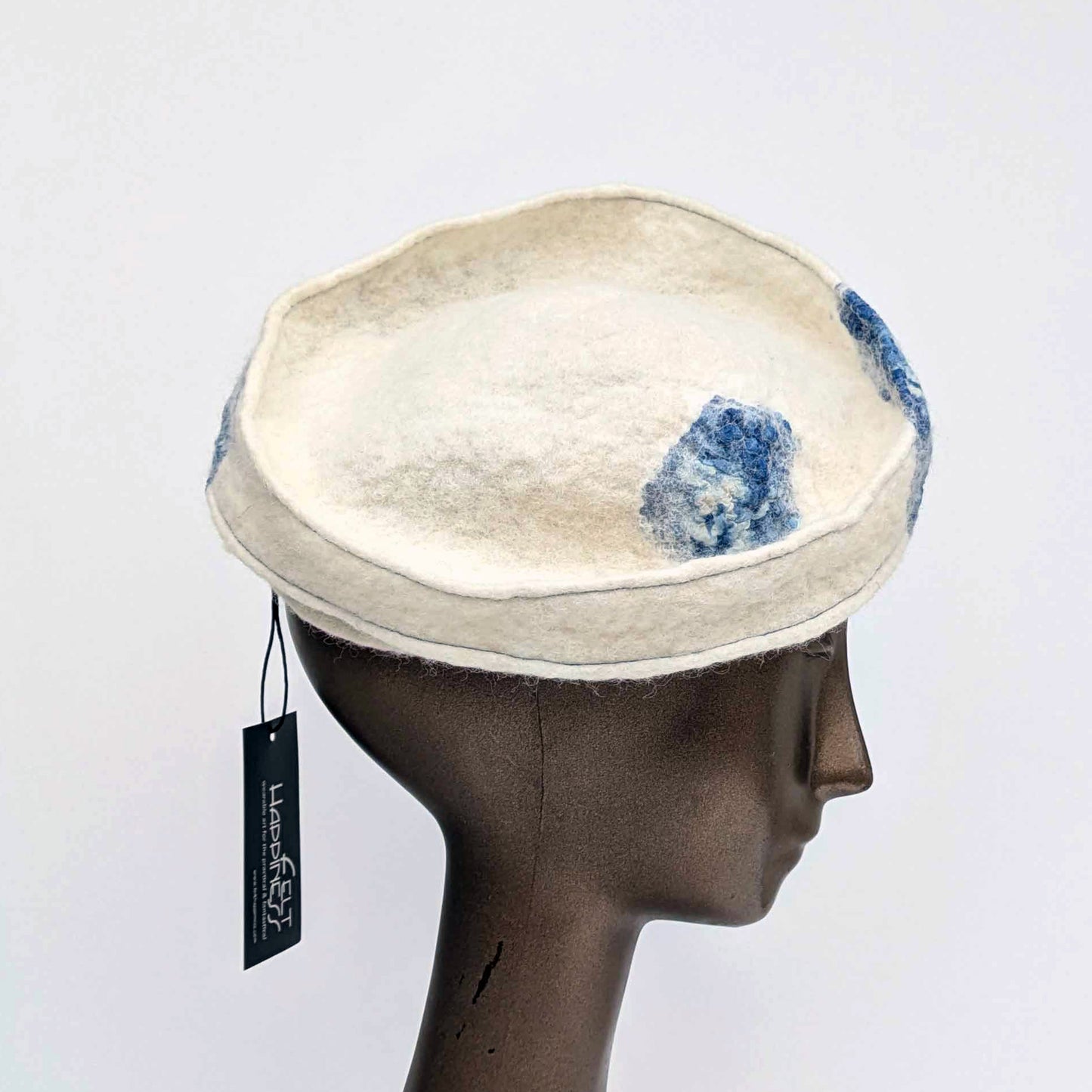 Cream-coloured fascinator hat with blue seaweed cyanotype printed accents on a mannequin head against a white background