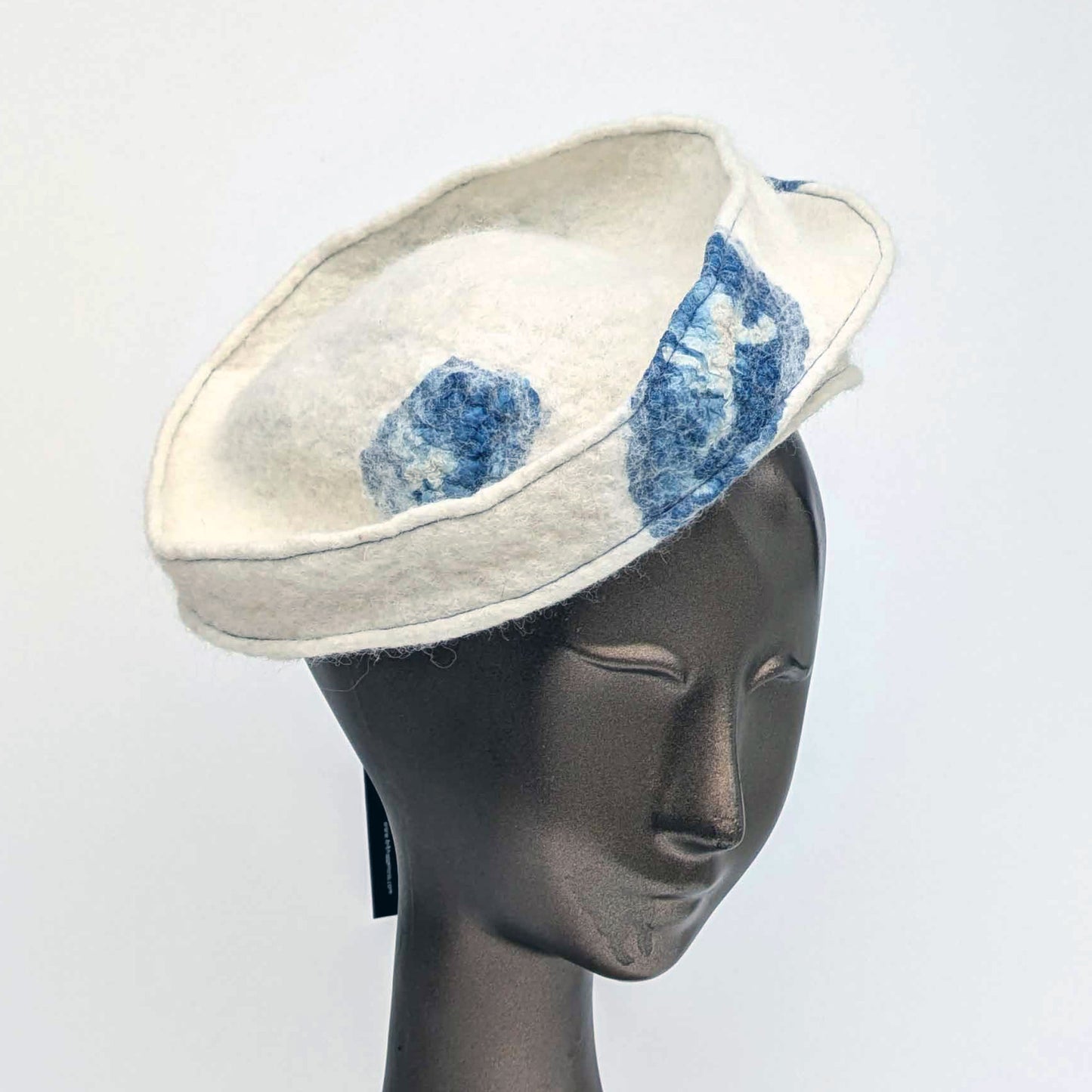 Cream-coloured fascinator hat with blue seaweed cyanotype printed accents on a mannequin head against a white background