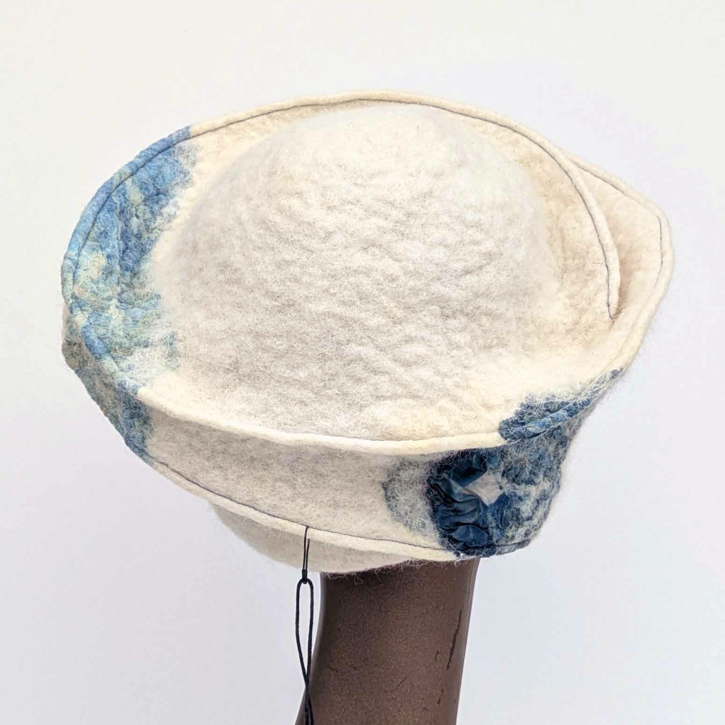 Cream and blue patterned, asymmetrical hat on a mannequin head against a white background - backview.