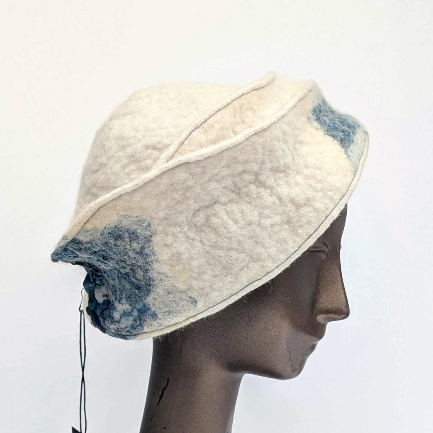 Cream and blue patterned, asymmetrical hat on a mannequin head against a white background -sideview.