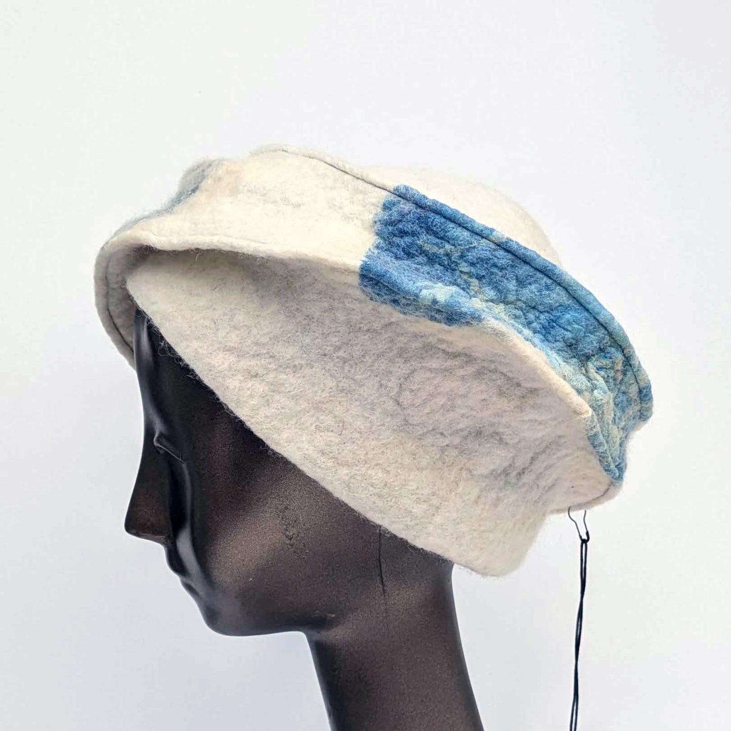 Cream and blue patterned, asymmetrical hat on a mannequin head against a white background - sideview.