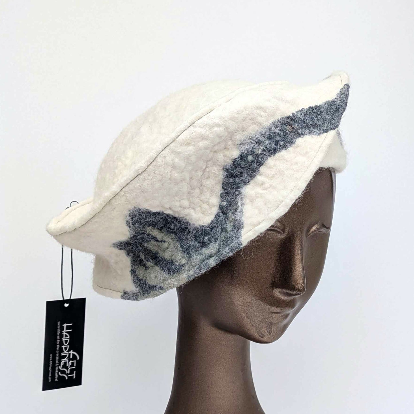 Cream coloured, asymmetrical hat with a broad band, with dark blue decorations - threequarters view.