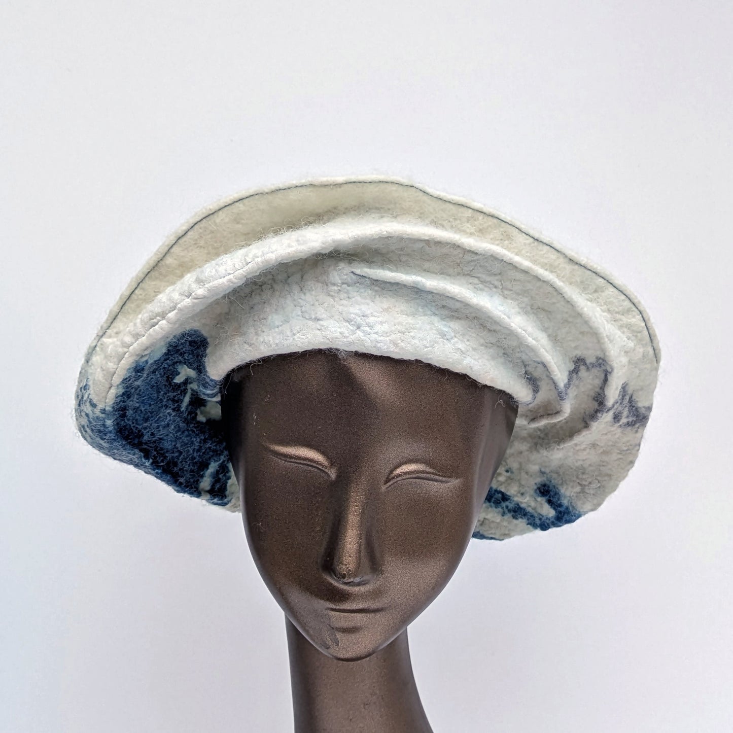 Creamy white felted hat with navy blue cyanotype printed seaweed towards the back of the hat.