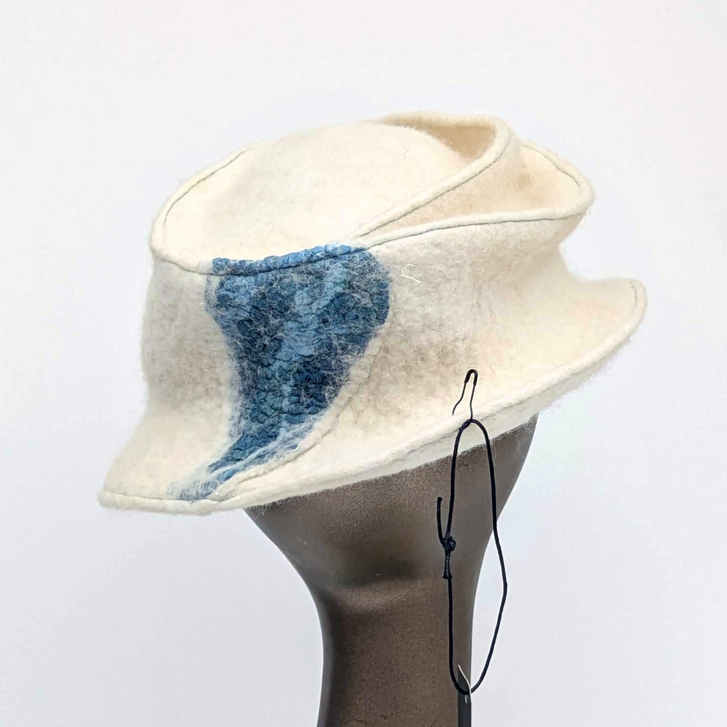 Cream coloured fedora with teal blue seaweed decorative element on the back.