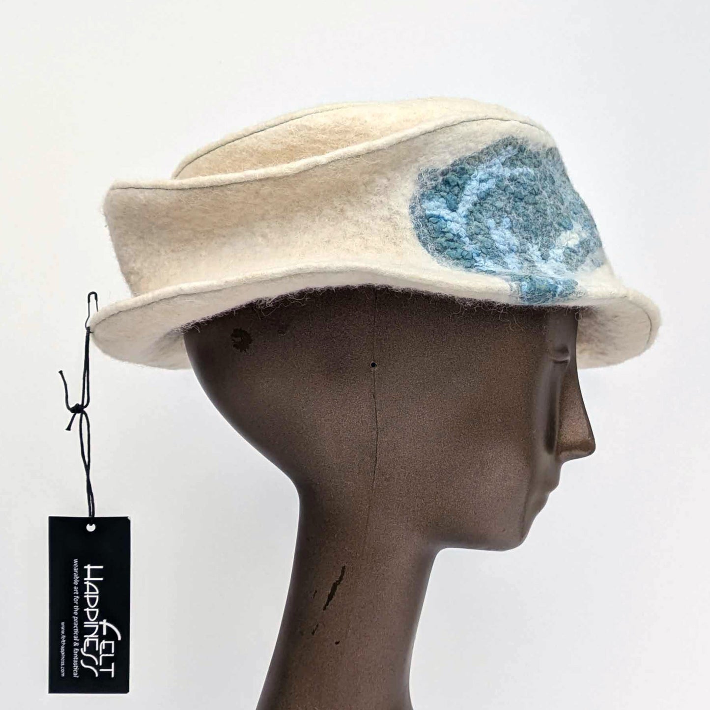 Cream coloured fedora with teal blue seaweed decorative element toward one side.