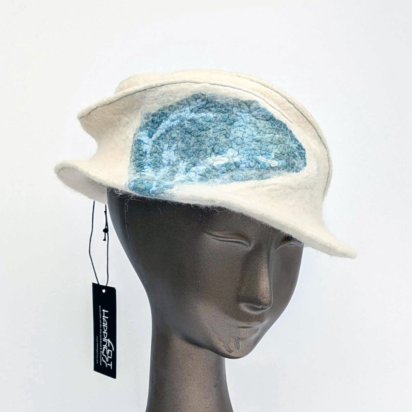 Cream coloured fedora with teal blue seaweed decorative element toward one side.