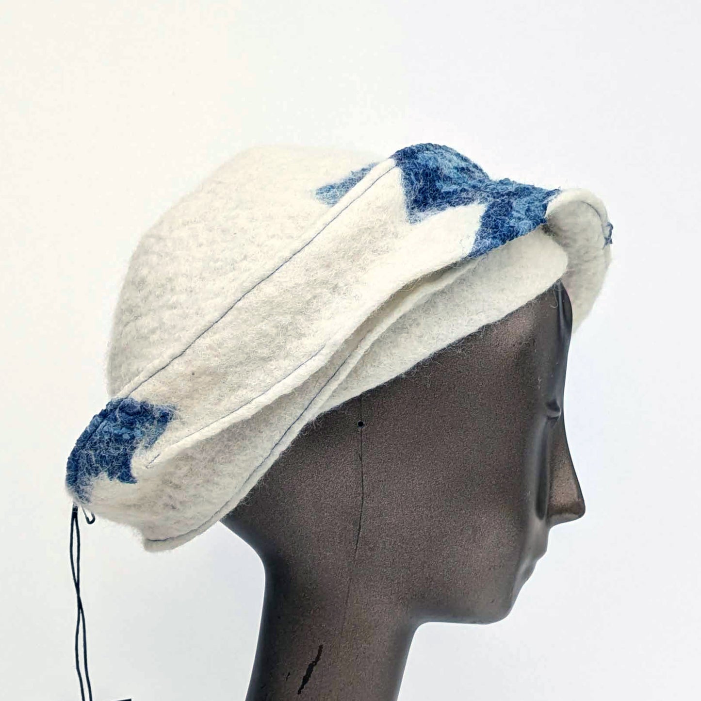 White cap with small bill and blue decorative elements on a mannequin head against a white background
