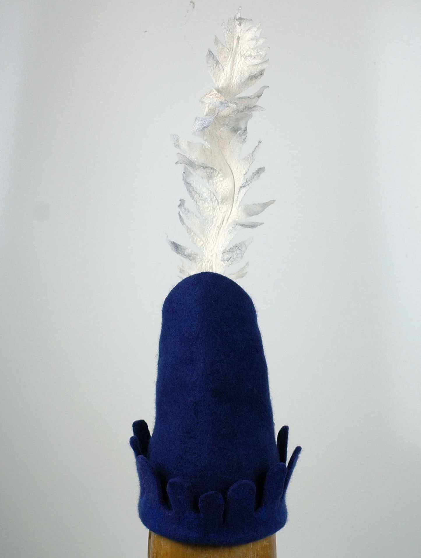 Blue Medieval Inspired Hat with detachable white feather in a gray felted vase. - back view