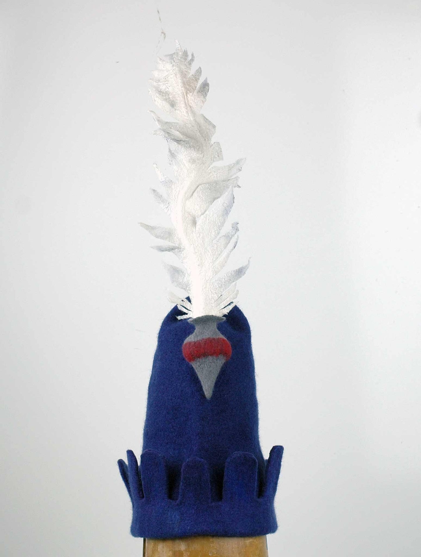 Blue Medieval Inspired Hat with detachable white feather in a gray felted vase. Front view.