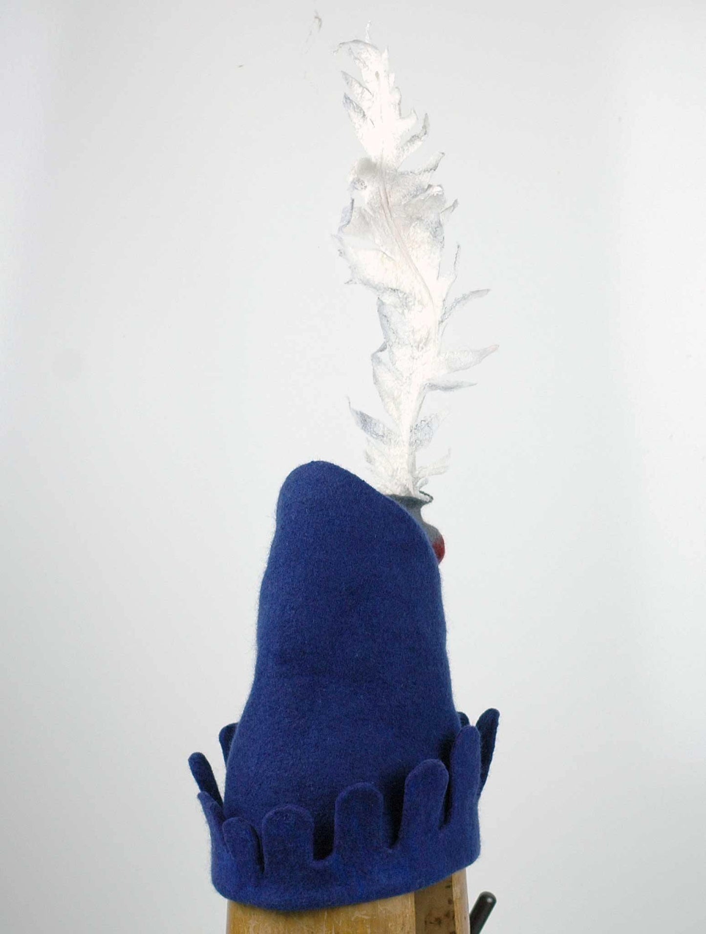 Blue Medieval Inspired Hat with detachable white feather in a gray felted vase. - side back view