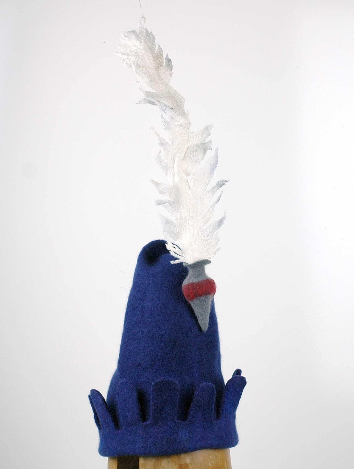 Blue Medieval Inspired Hat with detachable white feather in a gray felted vase. - threequarters view