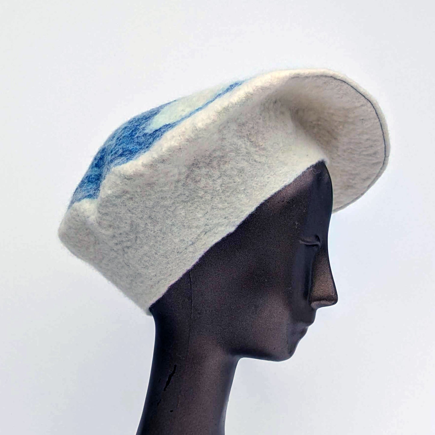 Mannequin head wearing a felted  white beret with blue accents on a light gray background