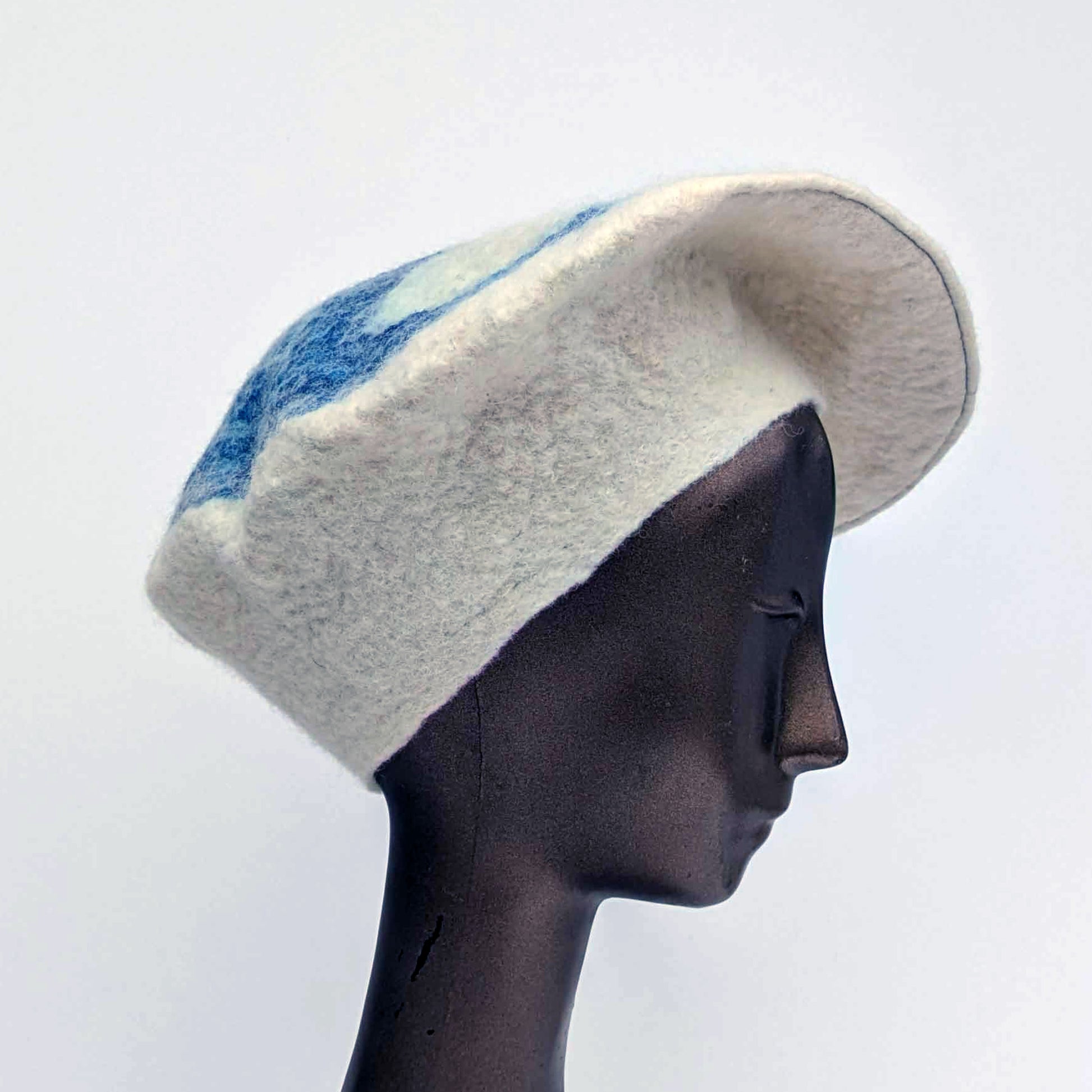 Mannequin head wearing a felted  white beret with blue accents on a light gray background