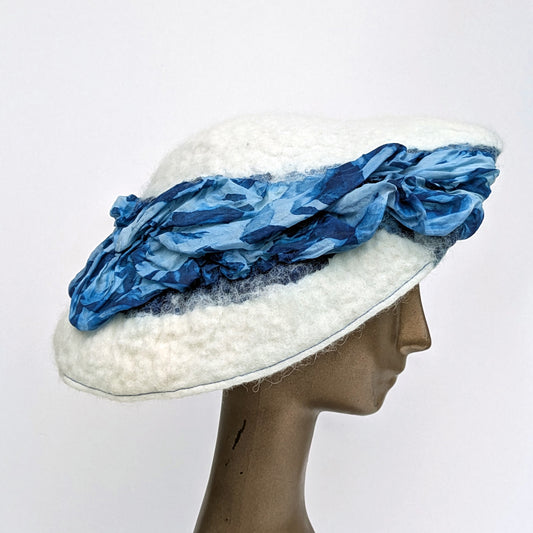 White angled beret with raised puffy blue silk fabric 'river' running across the hat.
