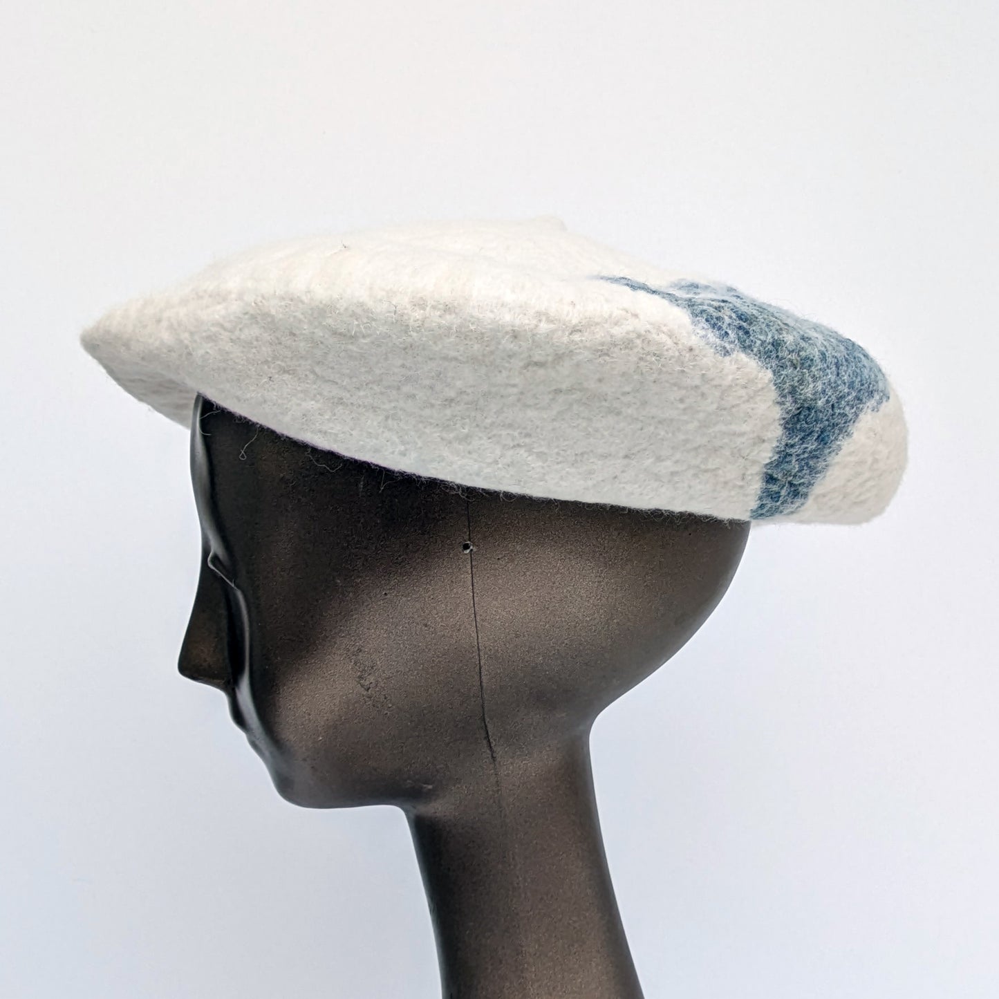 White beret with blue-green fabric towards the back of the hat  - worn by a mannequin