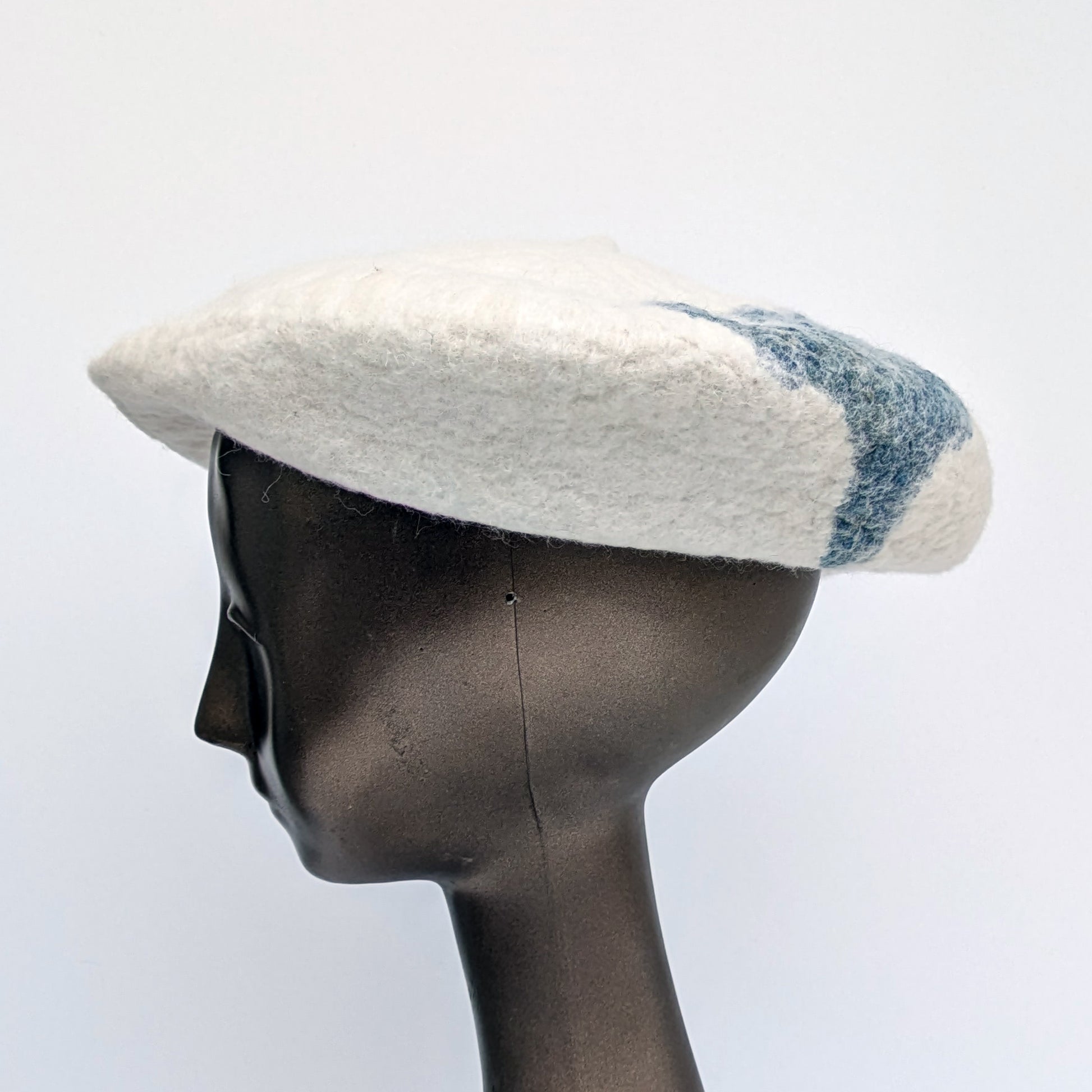 White beret with blue-green fabric towards the back of the hat  - worn by a mannequin