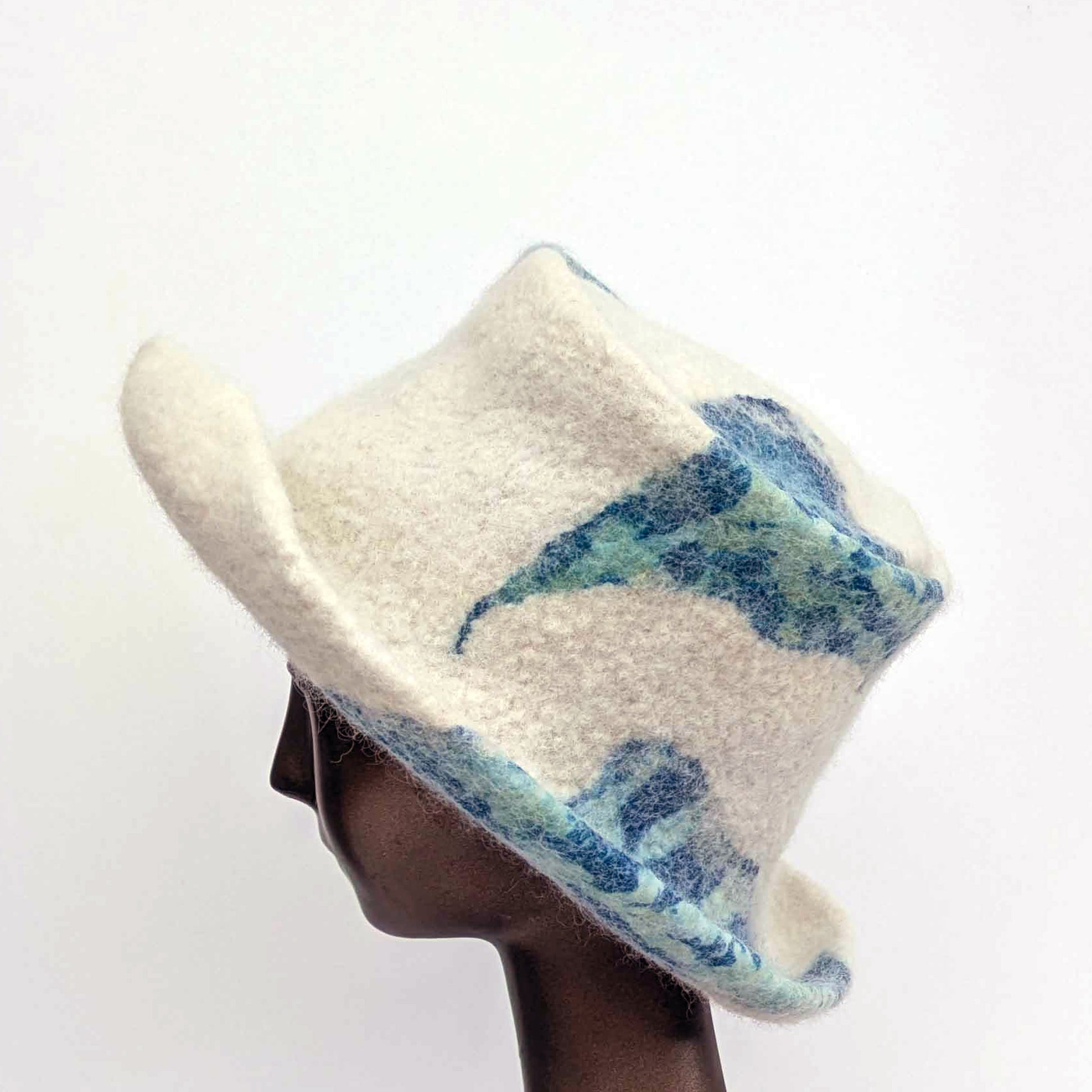 Cream-coloured top hat with wide brim and sage green seaweed print against blue Cyanotype -side view