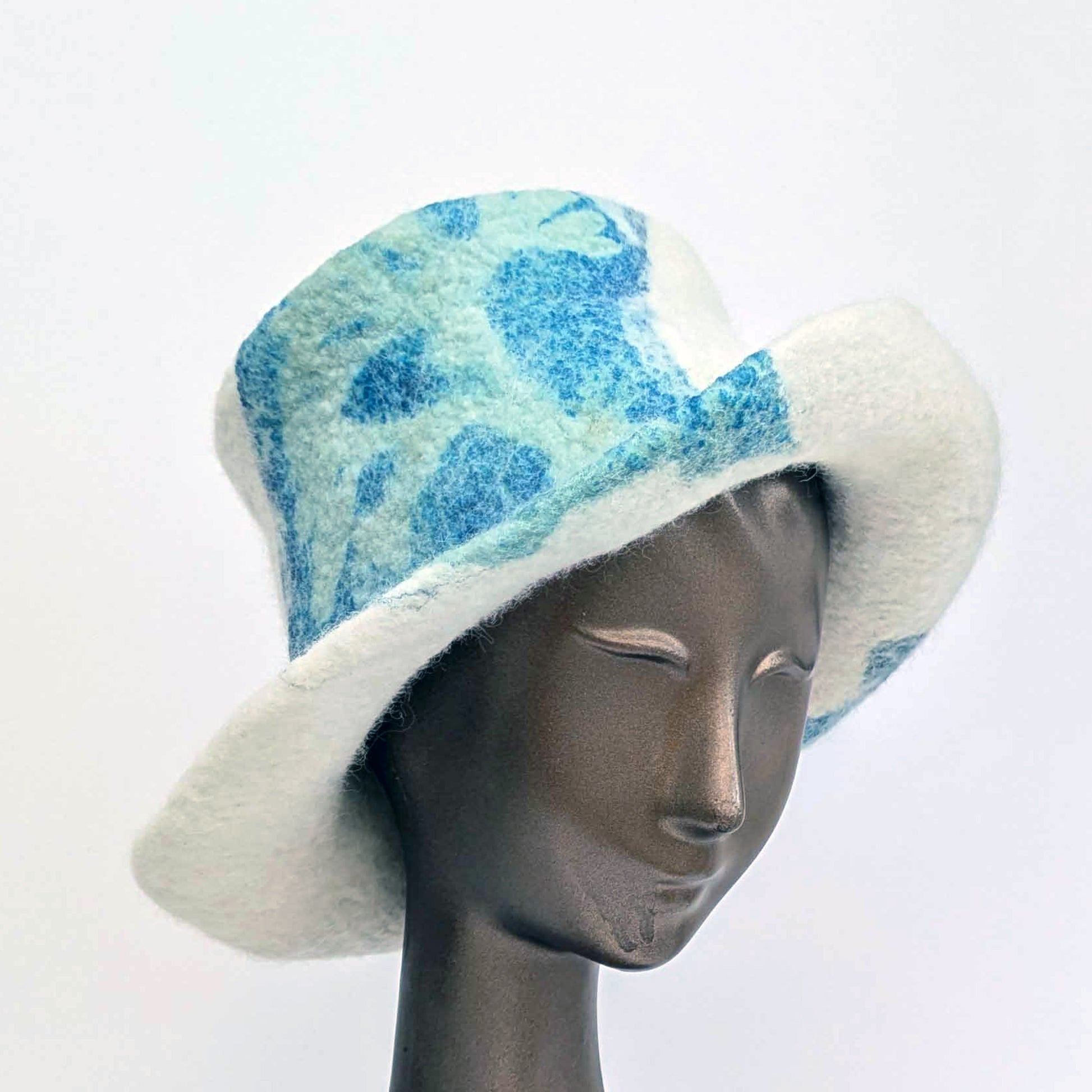 Cream-coloured top hat with wide brim and sage green seaweed print against blue Cyanotype - threequarters view
