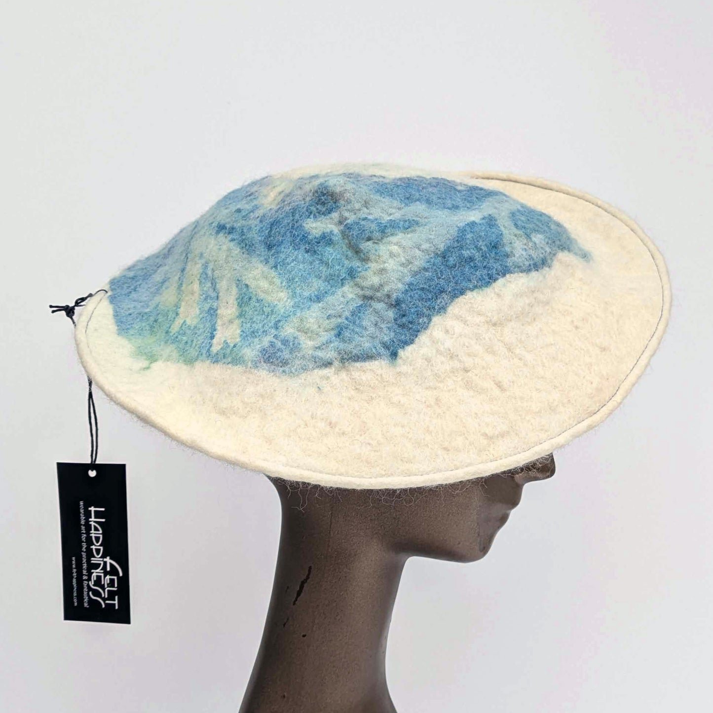 Cream coloured saucer beret hat with blue seaweed Cyanotype print on the tip - worn by a mannequin. Sideview.