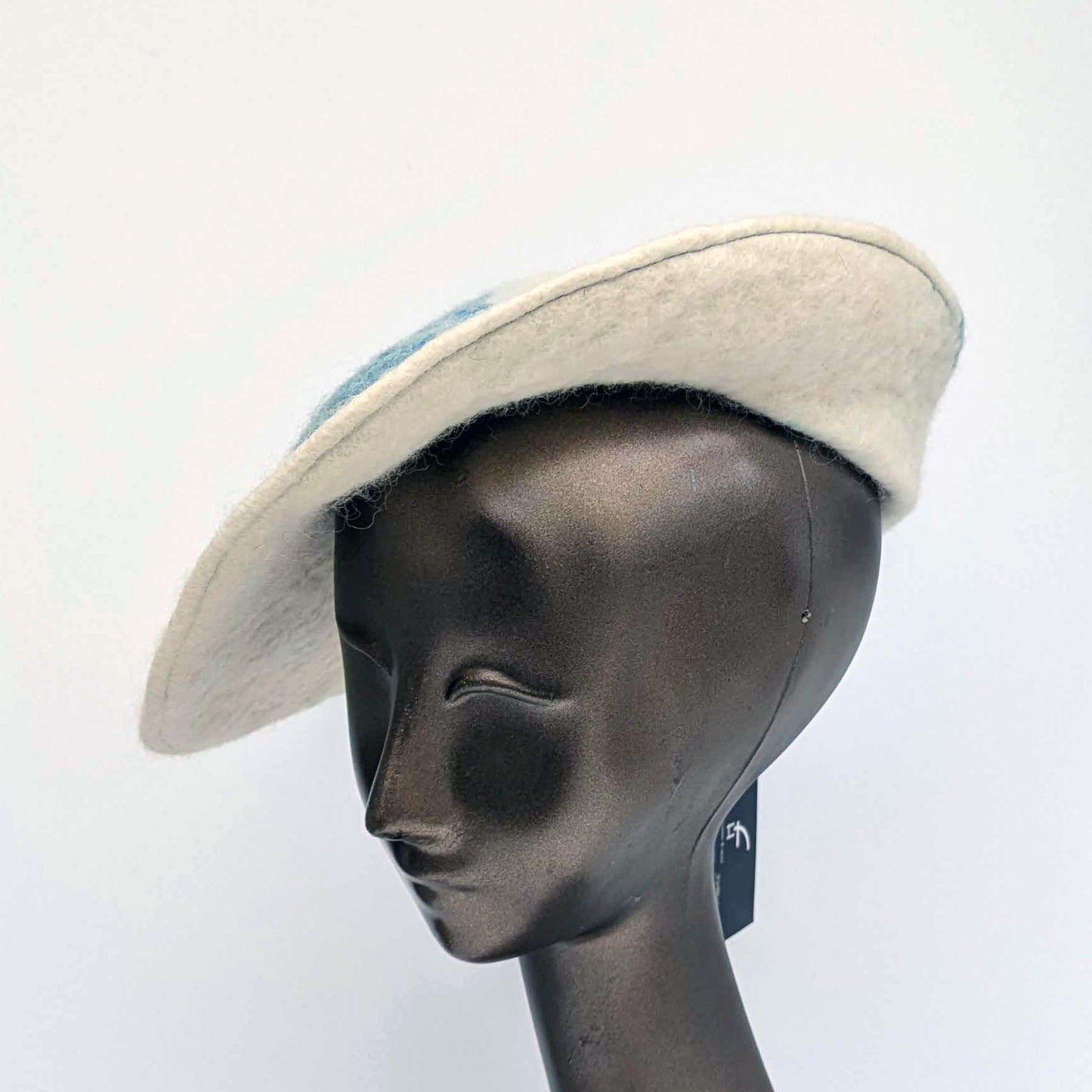 Cream coloured saucer beret hat with blue seaweed Cyanotype print on the tip - worn by a mannequin. Threequarters view