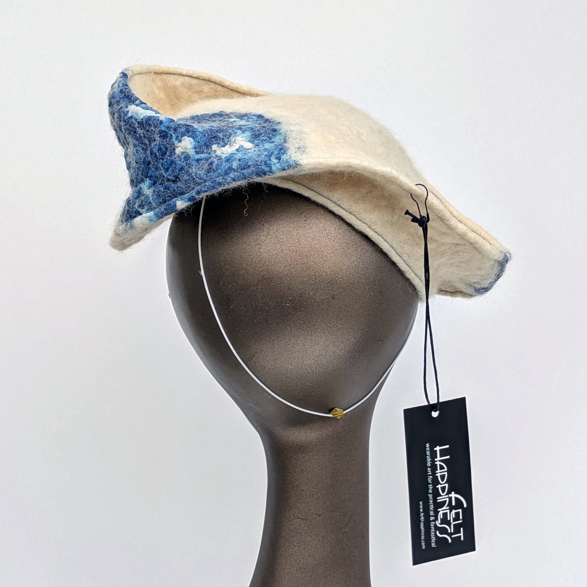 Cream and blue patterned fascinator on a mannequin head against a white background