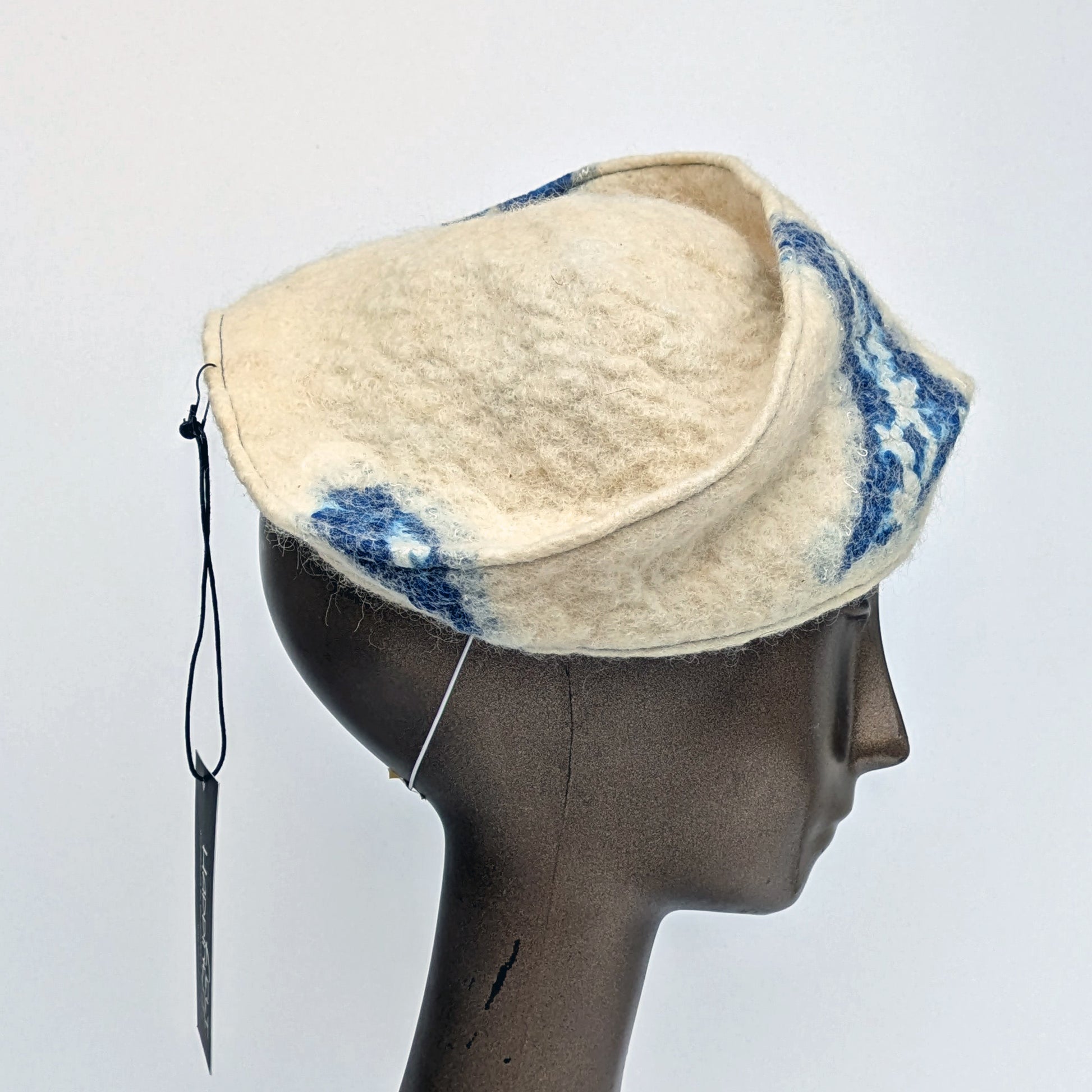 Cream and blue patterned fascinator on a mannequin head against a white background