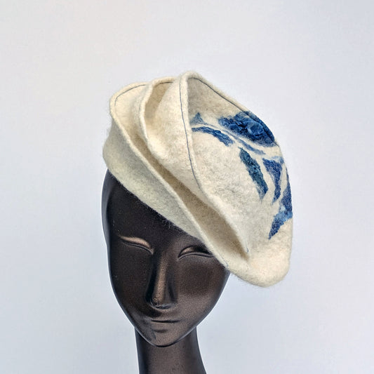 Small cream-coloured hat with blue stitchig and blue geometric patterning.