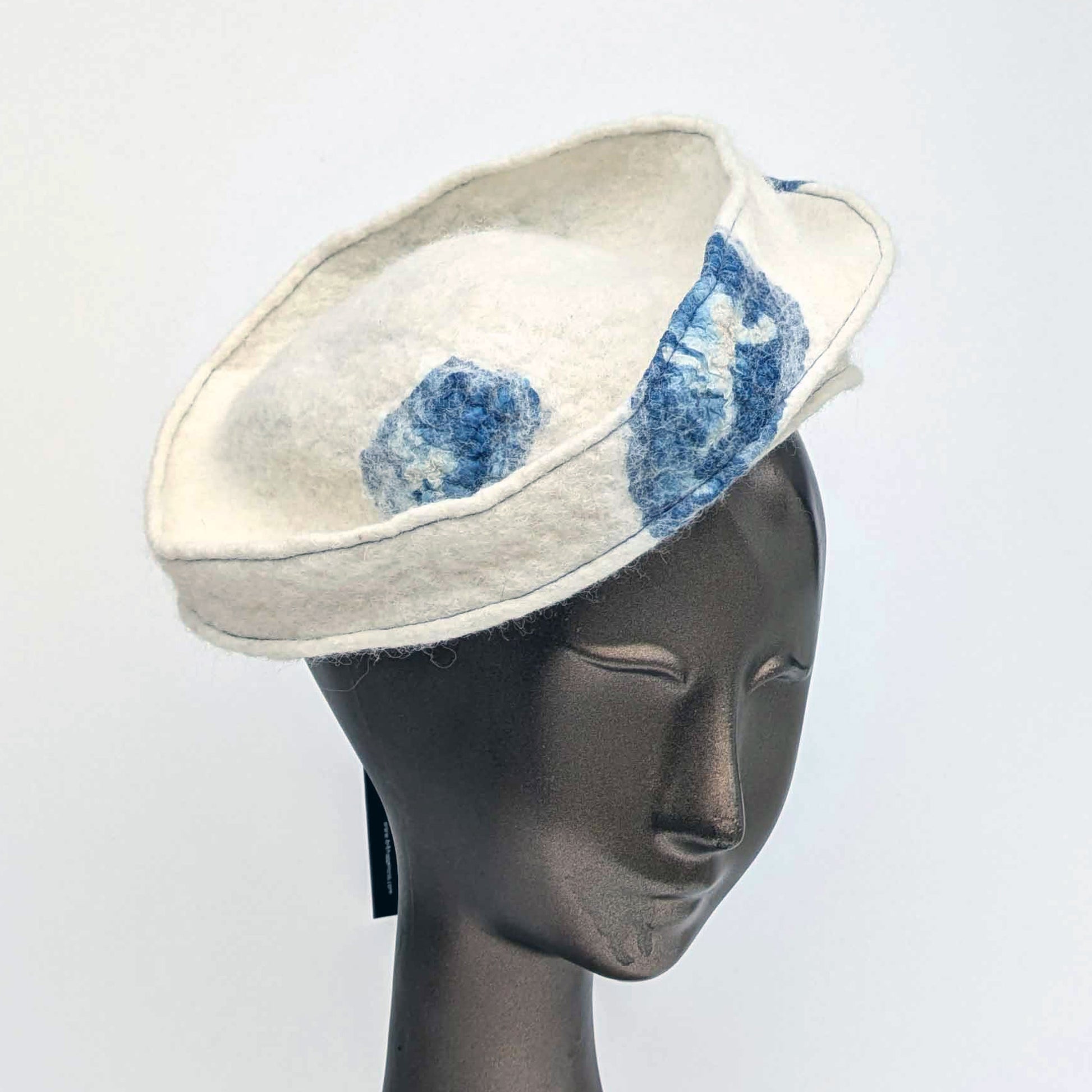 Cream-coloured fascinator hat with blue seaweed cyanotype printed accents on a mannequin head against a white background