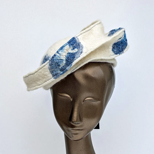 Creamy white hat with indigo blue silk patterning, that perches on the head at an angle.