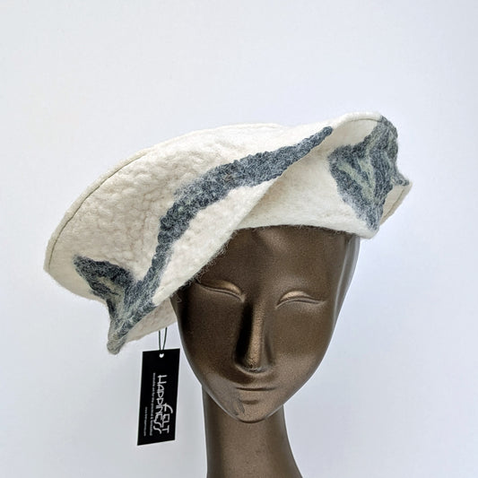 Asymetrical hat in creamy white with dark blue undulating silk fabric which spirals around the sides.
