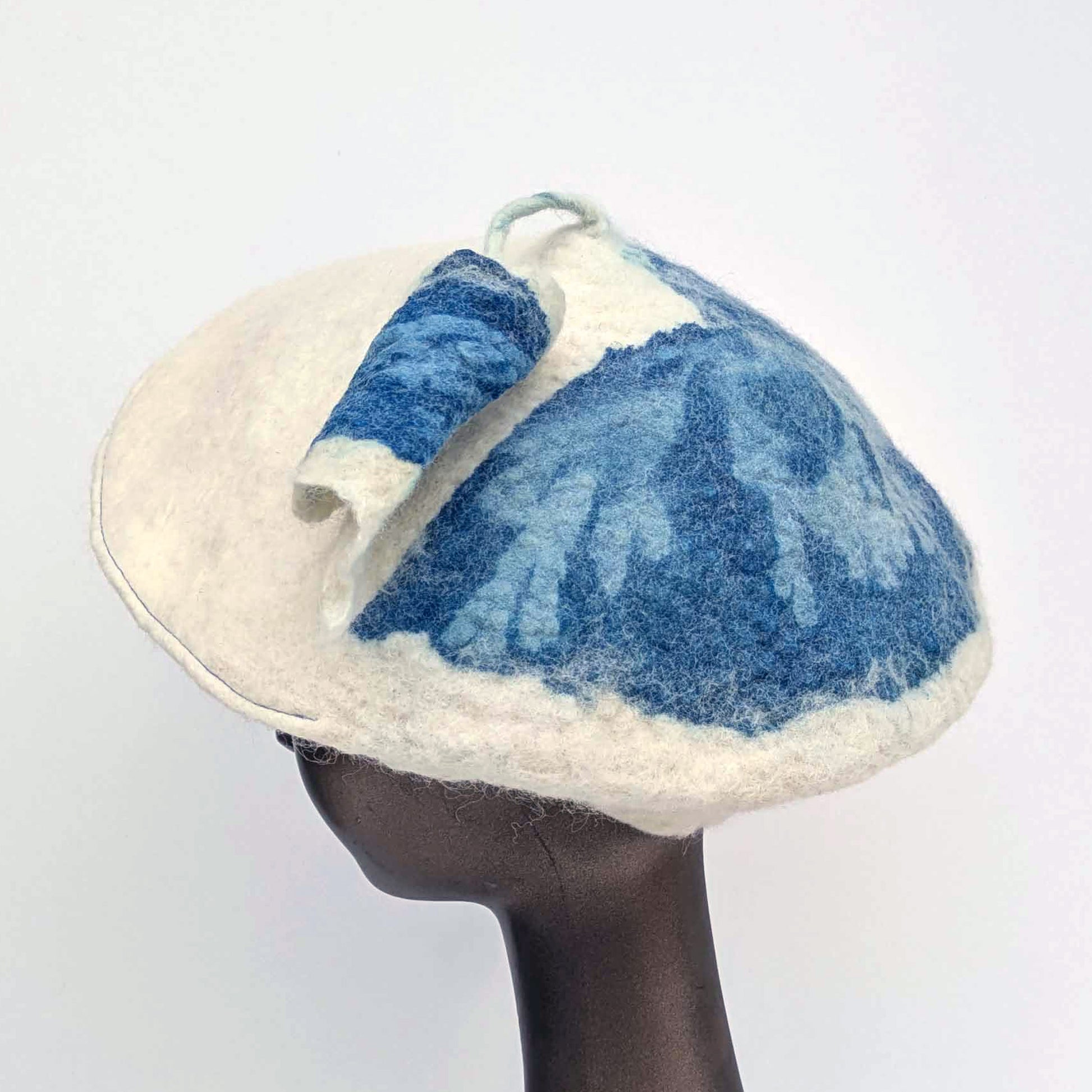 Seaweed blue printed cyanotype fabric on the side of a white coloured beret - with tassel. Worn by a mannequin.