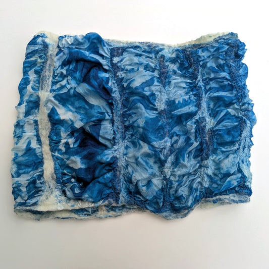Rectangular shaped felted cowl with a ruffled surface in blue and cream-coloured wool.