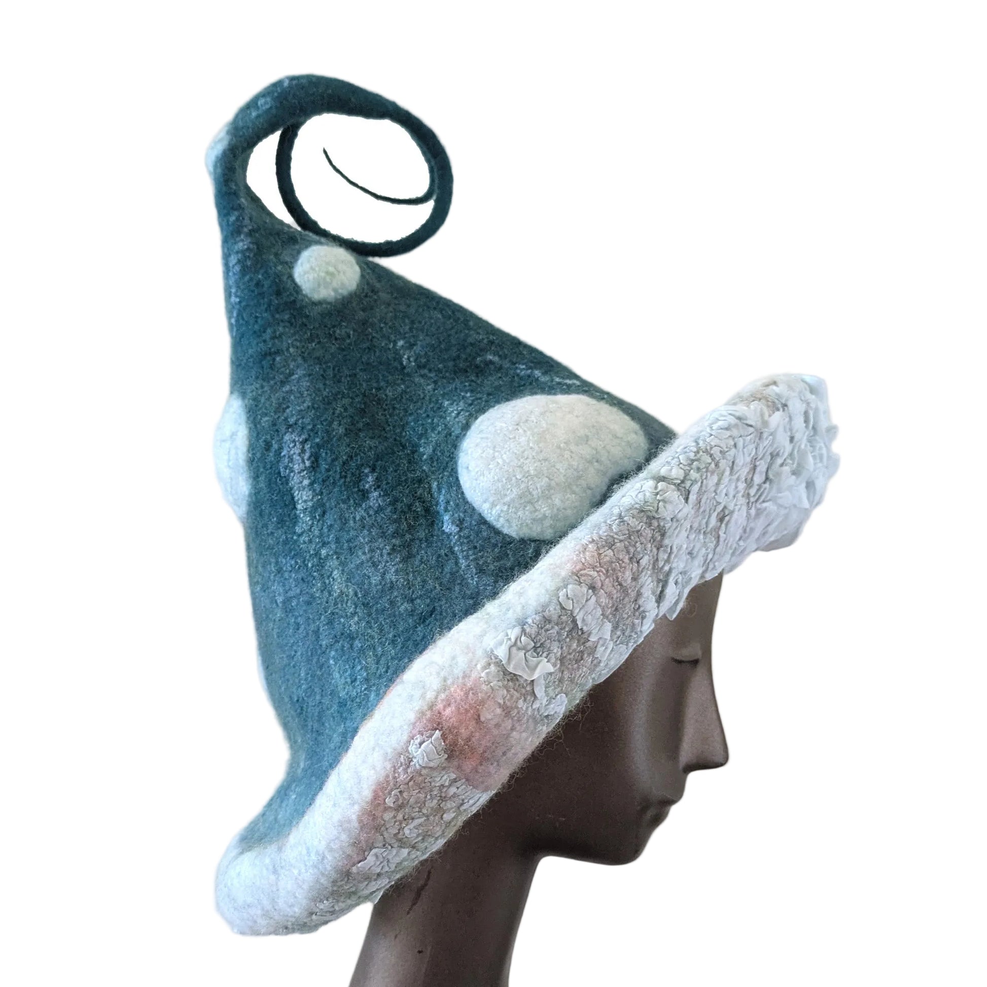 A felted mushroom-shaped hat displayed on a dark mannequin head against a plain beige background. The hat is dark blue-green with white felted spots in different sizes  and a ruched silk under-brim