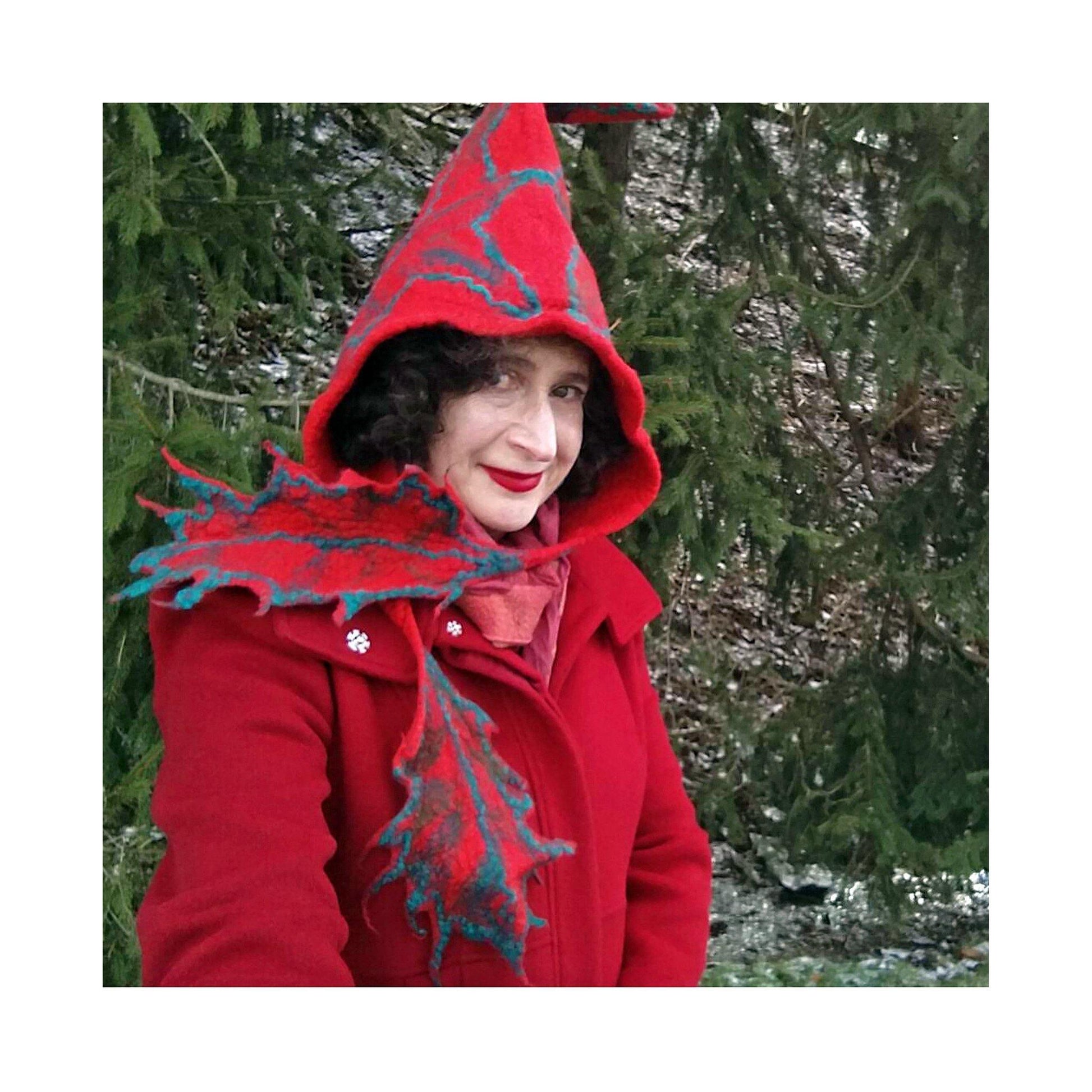 Red Felted Hood with holly ties in front of pine trees.