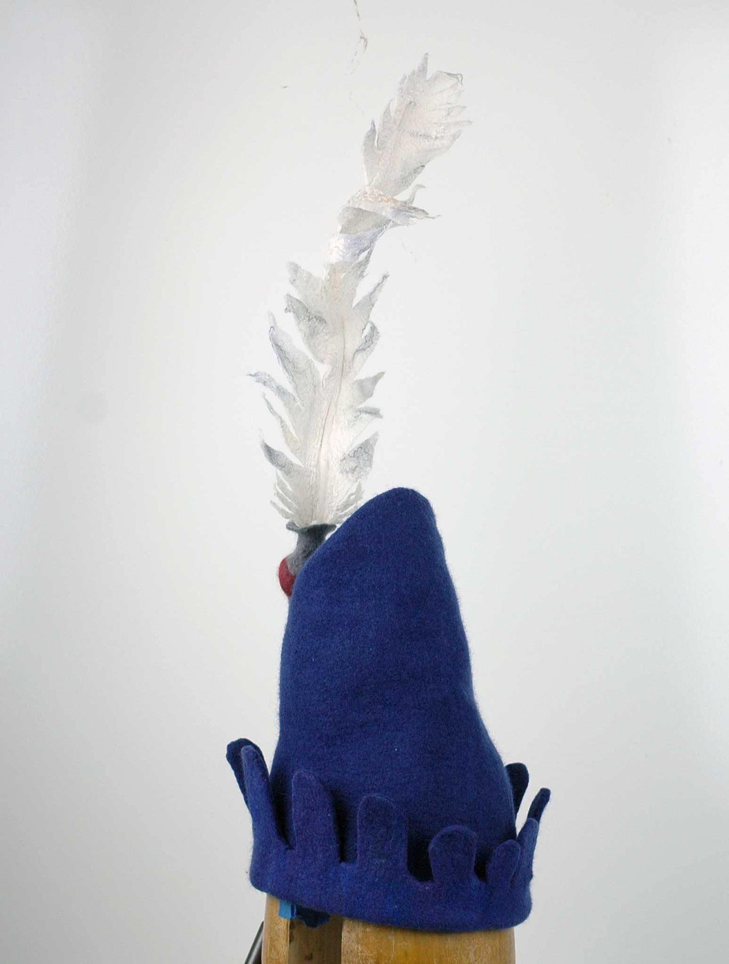 Blue Medieval Inspired Hat with detachable white feather in a gray felted vase. back view