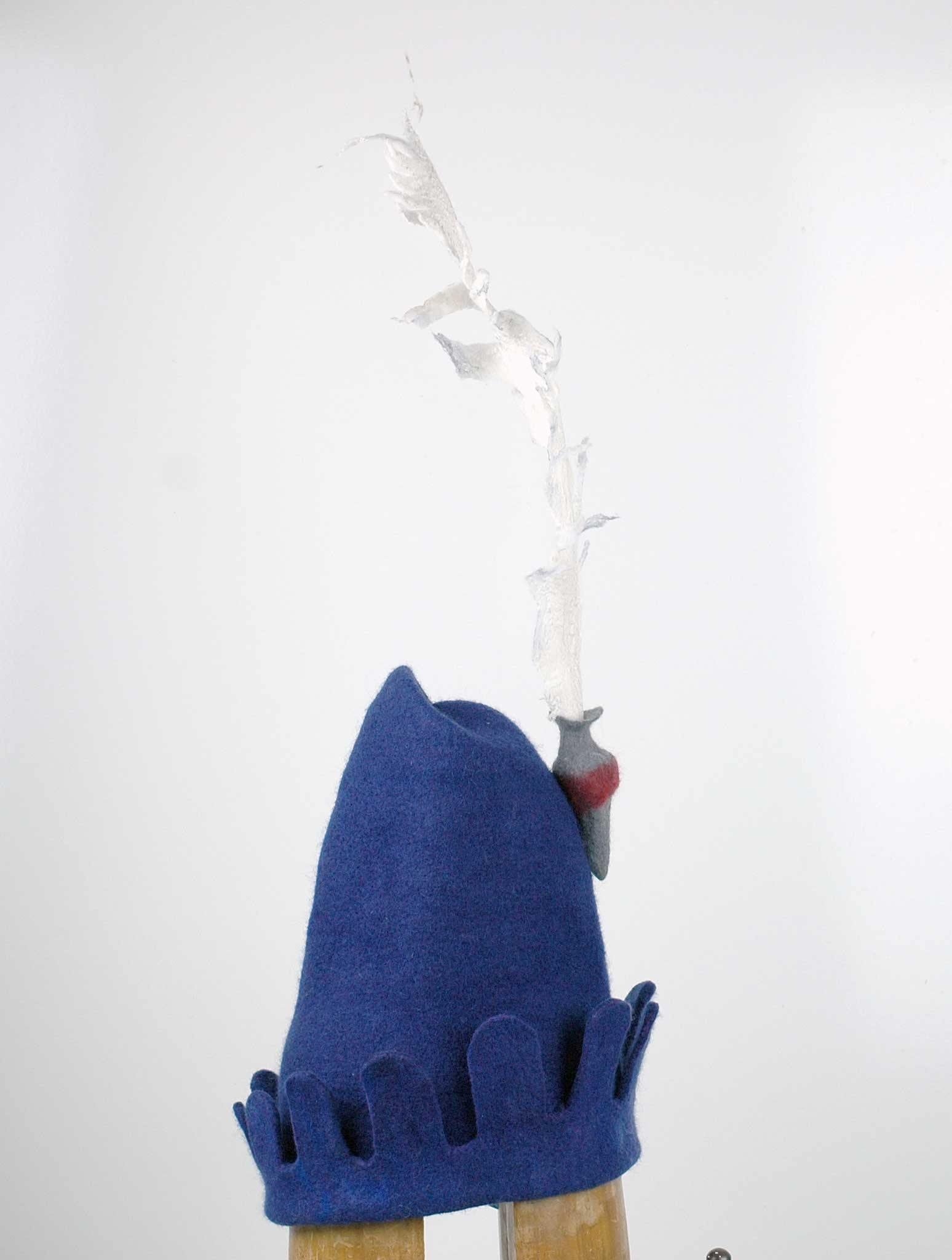 Blue Medieval Inspired Hat with detachable white feather in a gray felted vase. - side view