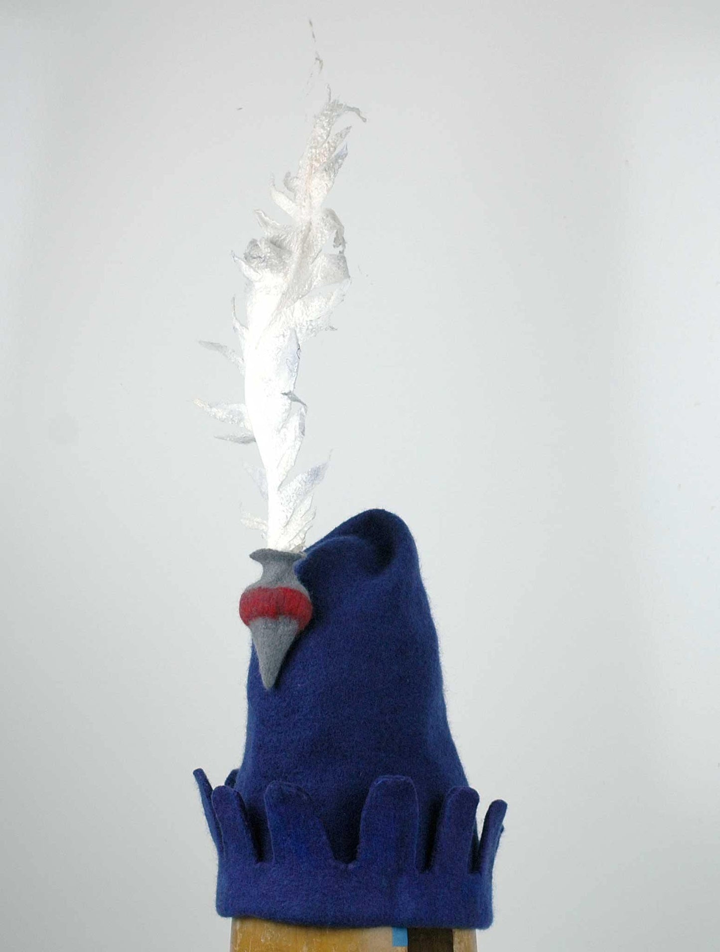 Blue Medieval Inspired Hat with detachable white feather in a gray felted vase. - threequarters view